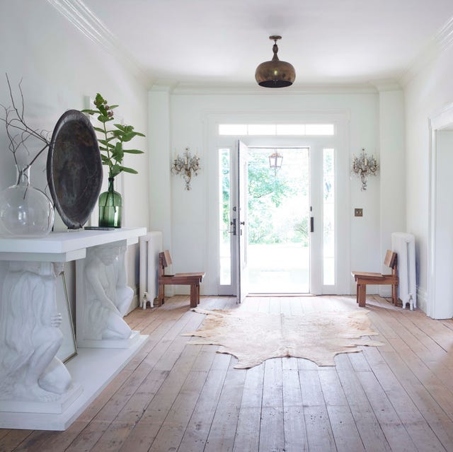 spare entry way with bleached wood flors and a white console with caryatid like pediments and a mirror over it and a shaggy green piece of artwork opposite