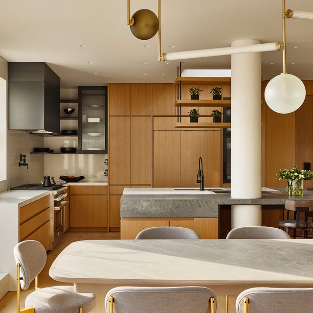 a kitchen with a long rounded edge light wood dining table with matching chairs and honey colored cabinets in the back