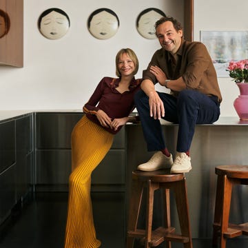 A couple poses in a modern kitchen, highlighting their attire and the surrounding decor.