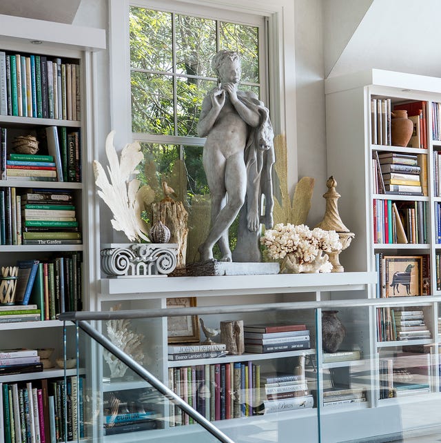 glass wall staircase with a landing made of built in bookcases full of books and a classical statue at center