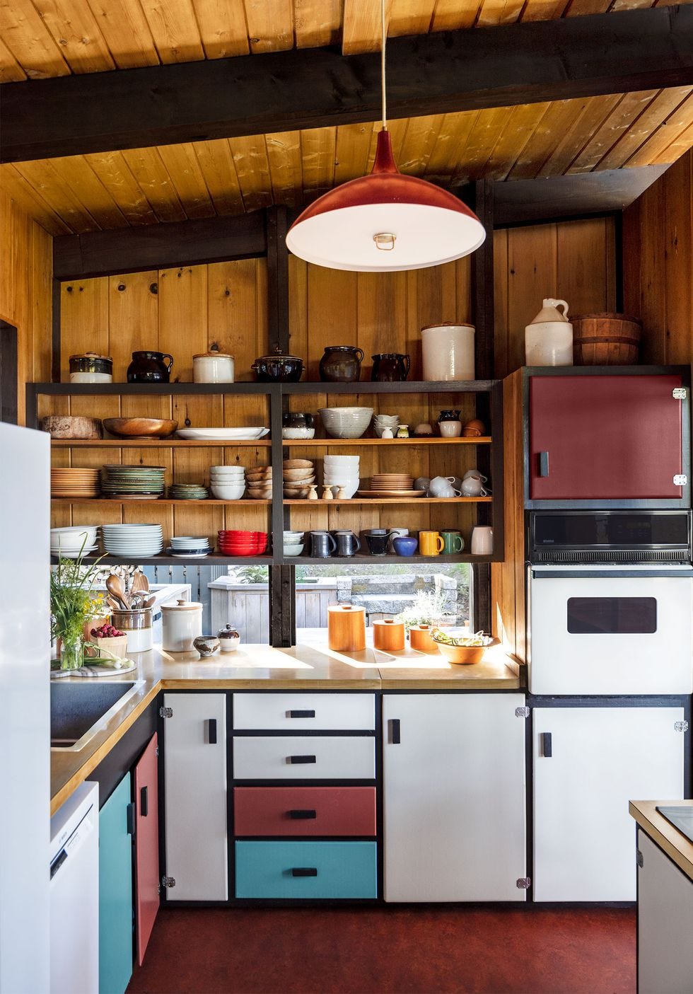 a kitchen with a red floor, exposed dinnerware on shelves, and wood paneling