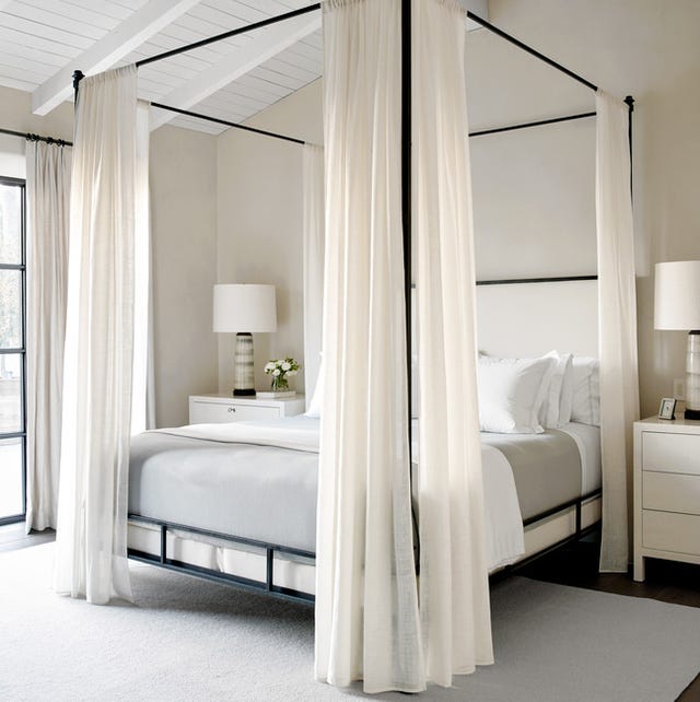 a four poster bed with white bed curtains and a large square rug