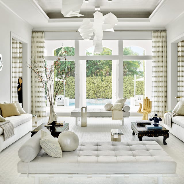 a all white living room with matching white sofas facing each other and a chaise longue in the foreground with a large window opening to a pool in the back and mat