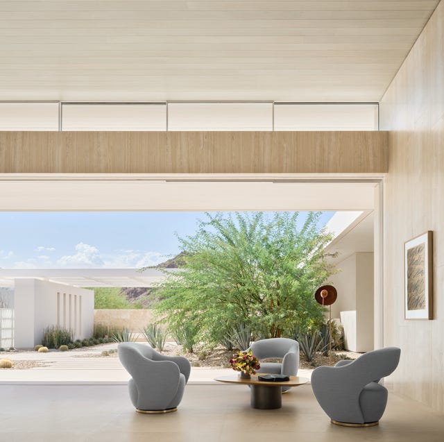 large open living area with three gray chairs around a low pedestal cocktail table and a large bushy tree in the opening