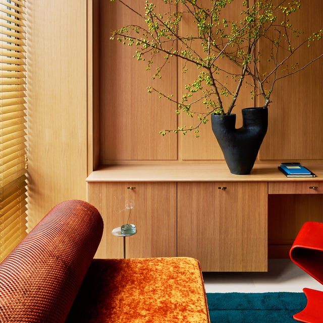 details of pale honey colored built in cabinetry with a black vase and branches on it and a bed in the foreground with an orange and blue modern bed with roll head and a red lacquer potato chip type chair peeking out from the right