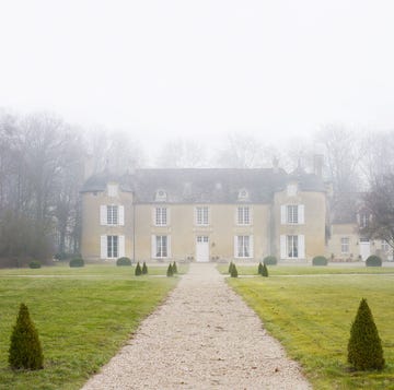elegant stone manor surrounded by mist with a gravel pathway and manicured shrubs