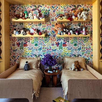 a child's bedroom with built in yellow cabinets and storage, bright flower print wallpaper, four yellow shelves filled with small stuff animals, two wood frame twin beds with tan covers, nightstand between beds