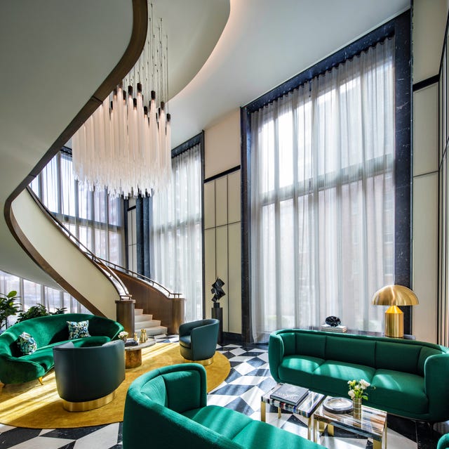 dramatic double height curtained living area with a sensuous curved staircase leading upstairs and a black and white tile floor and green curvy sofas and a yellow carpet