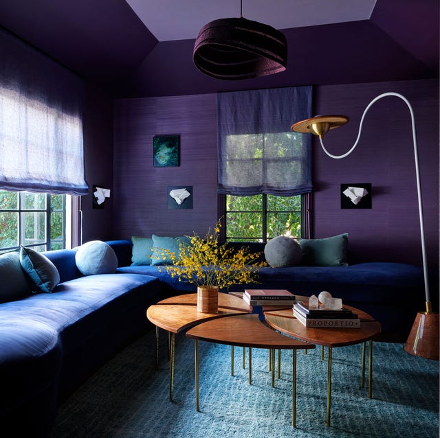 a living room with dark purple walls and a dark blue wraparound sofa and round sectional coffee table and a swooshy standing lamp
