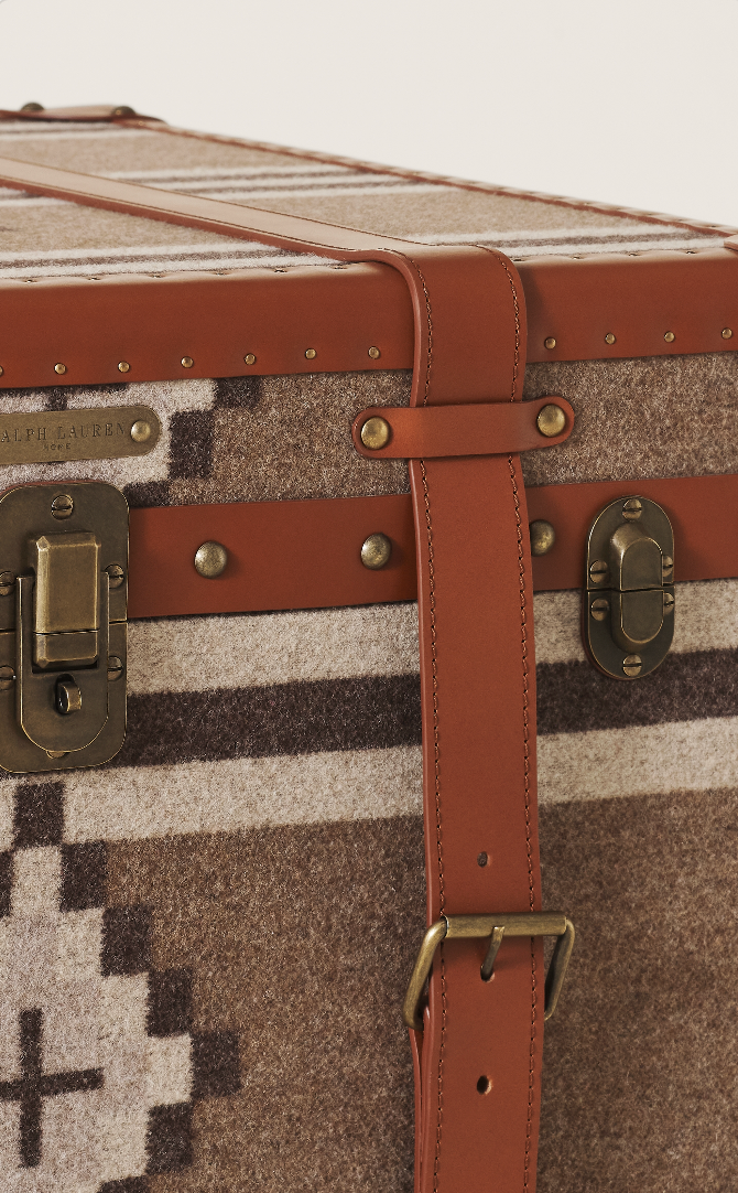 A wool travel trunk with leather straps and brass hardware.